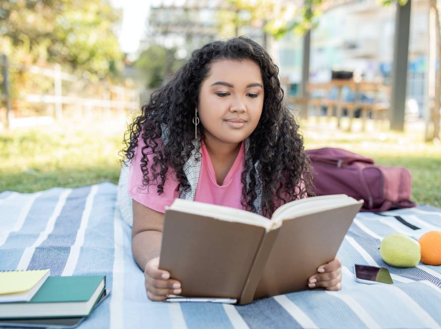 Hispanic Student Woman Learning Reading Book Outdoors Lying On Blanket